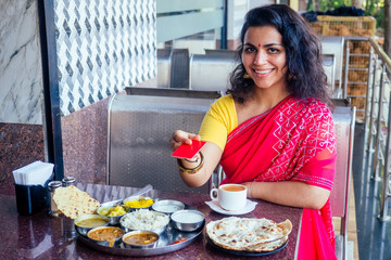 beautiful brunette woman in red sari paying by plastic card for traditional thali with...
