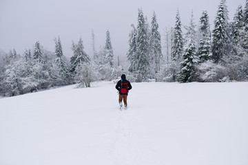 Hiker walking alone through snow covered field in winter