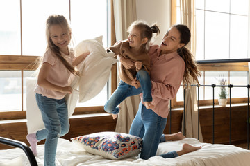 Happy mom and little daughters enjoying pillow fight on bed
