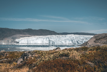 Greenland Glacier with Sea Ice and a Glacial Landscape near the Eqip Sermia Glacier, Eqi in Western Greenland near arctic town of Ilulissat. Blue sky on a sunny day. Calving Glacier.