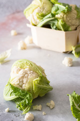 Fresh cauliflower tops on stone surface. In the background a box containing other cauliflowers just bought at the market. Fresh vegetables for healthy vegetarian and vegan cuisine.