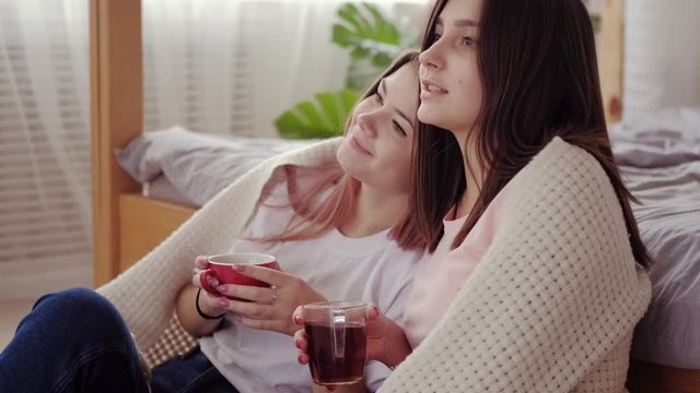Sisters leisure. Family bonding. Two happy teen girls enjoying hot drinks watching movie together.