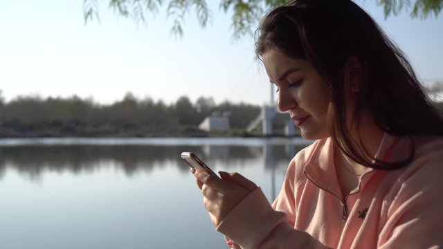 Beautiful girl with phone in the park near the lake.
