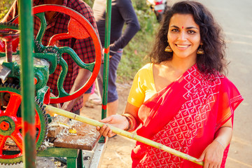beautuful induan woman in red sari standing near sugarcane juice maker apparatus machine , plantation summer farm background. small business start up