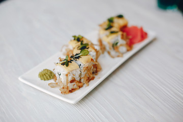 Sushi are on wooden table. Sushi are on white plate. Sushi served with wasabi and ginger.