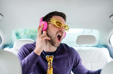 Cheerful man with party accessories sitting in car, having fun.