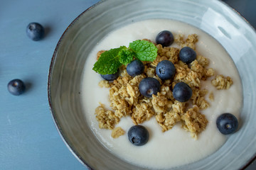 Food photography of a ceramic bowl with yogurt, granola cereal and blueberries on a blue background.