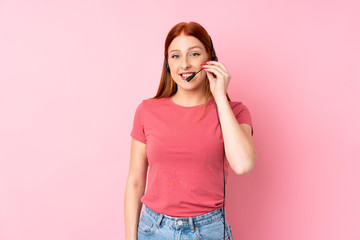 Young redhead woman over isolated pink background working with headset