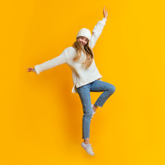 Playful winter girl having fun over yellow studio background