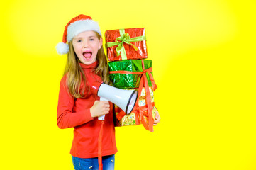 Girl in santa claus hat with box boxes in hand shouts into a megaphone, on a yellow studio background. Sales time
