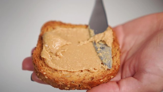 Girl smears a knife with juicy peanut butter homemade on a grain toast closeup. Making Healthy Organic Breakfast
