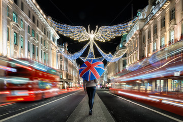 Eine Touristin läuft durch das weihnachtlich geschmückte Zentrum von London und hält einen Regenschirm mit Britischer Flagge, Großbritannien