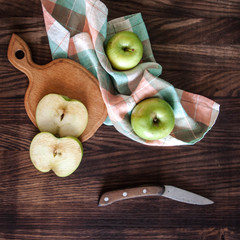 Green apples with sliced board, knife and cloth on wooden background