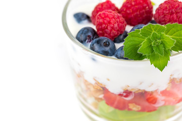 Portion cup with yogurt and muesli. Pieces of fruit are laid in layers, spilled with soys. Granola is decorated with mint leaf and fresh raspberry. White background. Copyspace