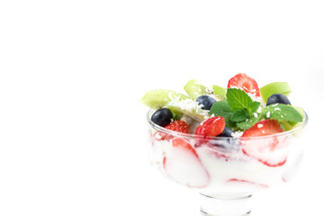 Portion cup with yogurt and muesli. Pieces of fruit are laid in layers, spilled with soys. Granola is decorated with mint leaf and fresh raspberry. White background. Copyspace
