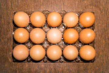 Fifteen brown eggs in a transparent plastic box look with faith. The image is in the background. Flat lay horizontally.