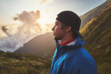 A young hiker in a blue jacket with orange backpack standing and looking up in the mountains,...
