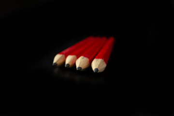 Four red pens placed one followed by another in perspective with plain black background