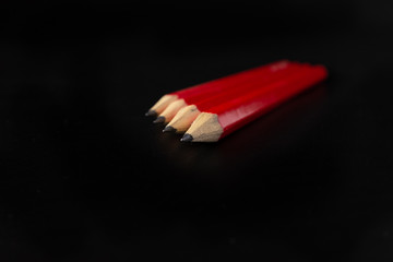 Four red pens placed one followed by another in perspective with plain black background