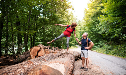 Senior tourist couple with backpacks walking in forest in nature.