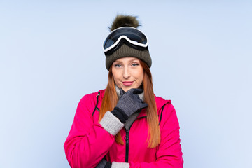 Skier redhead woman with snowboarding glasses over isolated blue wall laughing