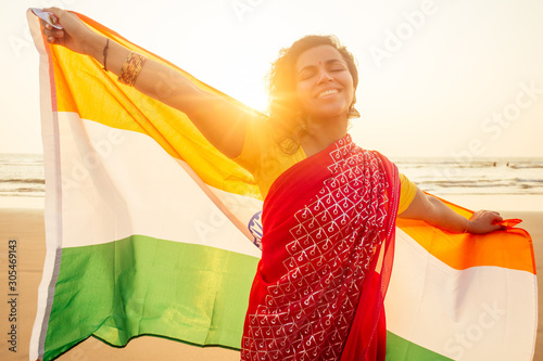 beautuful woman holding Indian flag tricolour ,wearing red tradition sari on sea beach in Goa