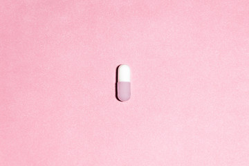 white and pink capsule on a pink background. the capsule is in the center.