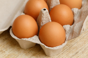 Brown chicken eggs in carton box on wooden table
