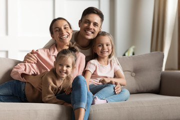 Smiling parents hug small kids daughters relaxing on couch, portrait