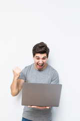 Emotional young man with laptop celebrating victory on white background