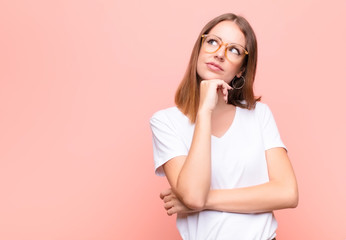 young red head woman feeling thoughtful, wondering or imagining ideas, daydreaming and looking up to copy space against flat wall