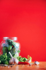Pickling cucumbers in cans. Ingredients for marinated gherkins, glass jar, garlic, dill, salt, pepper on red background. Copy space. Concept of vegetables preservation.