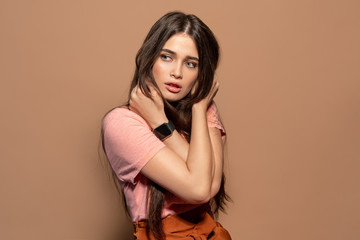 Fototapeta premium Freestyle. Young girl in top standing studio isolated on brown hugging herself looking aside pensive