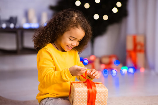 Curious little black girl opening gift box on Christmas Eve