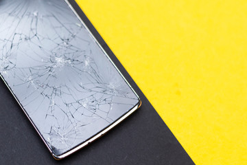 A broken phone on yellow and black background. Crushed device with broken screen representing an accident. Textured screen with damage. Dark glass of a screen.