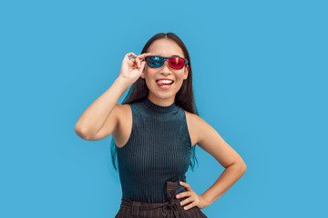 Freestyle. Young woman wearing 3d glasses standing isolated on blue posing to camera showing tongue playful