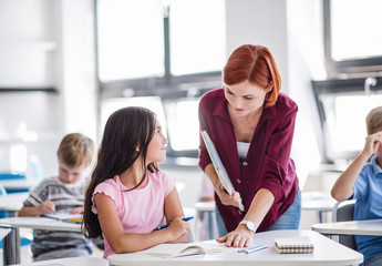 A teacher walking among small school children on the lesson, explaining.
