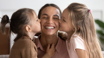Two cute adorable little daughters kissing happy mum on cheeks