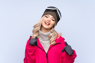 Skier teenager girl with snowboarding glasses over isolated blue background proud and self-satisfied
