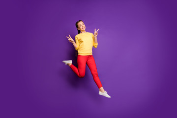 Fototapeta na wymiar Full length photo of pretty teen lady jumping high having fun showing v-sign symbols wear casual yellow pullover red trousers isolated bright purple color background