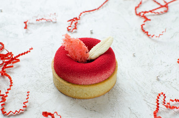 Contemporary raspberry mini mousse tart covered with red velvet spray decorated with chocolate feathers on light background