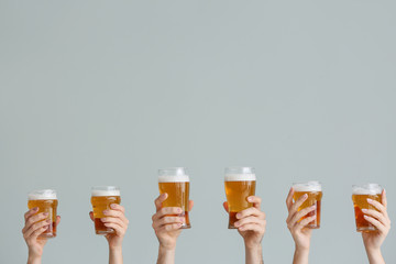 Hands with glasses of beer on grey background