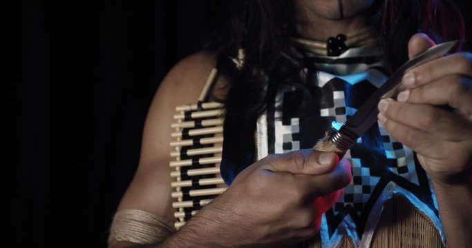 Cherokee man is holding a handmade knife, looking at it, face paint, close up