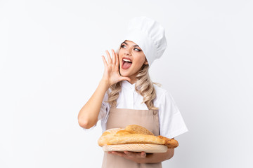 Teenager girl in chef uniform. Female baker holding a table with several breads over isolated white background shouting with mouth wide open
