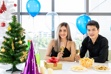 Attractive young man and woman celebrate Christmas and New Year in office party, clinking champagne glass, with snack and beverage on table