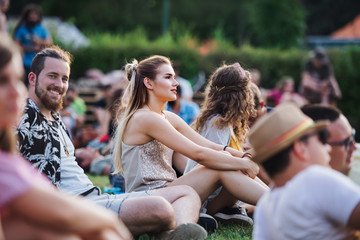Group of young friends sitting on ground at summer festival. - obrazy, fototapety, plakaty