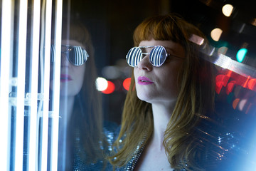 girl with sunglasses and fringe looking at neon lights