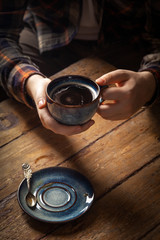 Fototapeta na wymiar Closeup black americano coffee in blue cup in male hand, saucer with vintage tea spoon on wooden brown vintage background. Concept breakfast in coffee house