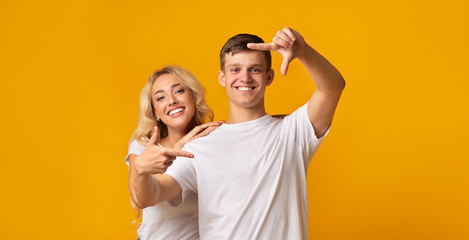 Cheerful millennial couple making frame with fingers, having fun together