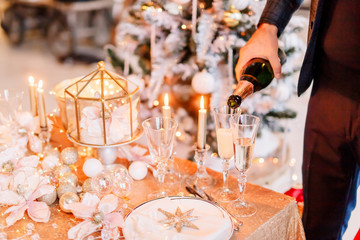 New Year 2020. New Year mood. Table with a gold tablecloth, decorated with candles and tableware for celebration. Festive still life by candlelight.A man pours champagne into a glass. Close-up.